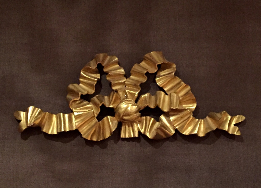 Ruban. En tilleul, sculpté et doré à la feuille d’or, dorure à l’eau avec brunissage à la pierre d’Agathe. Perruque autorisée, atelier de restauration du Château de Versailles, circa 1978. H. 28 x 44 cm.